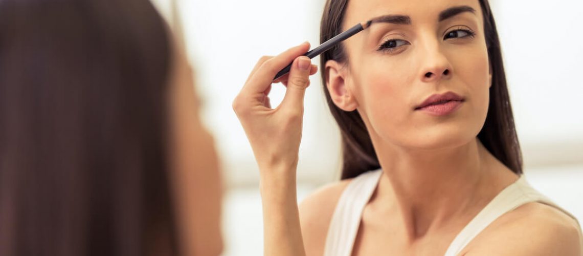 woman applying makeup to her eyebrows